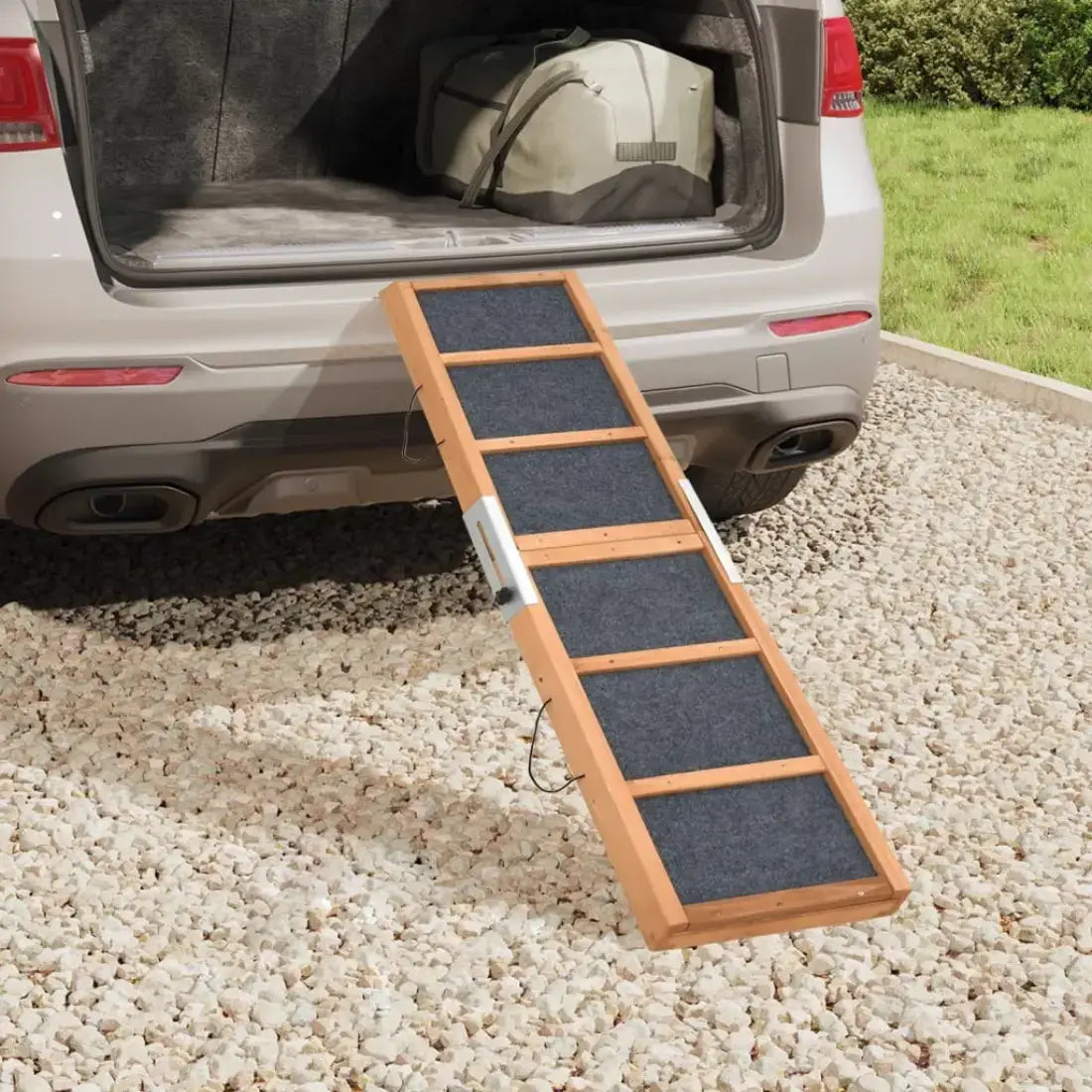 Pet ramp leading into an open car trunk on a gravel surface.